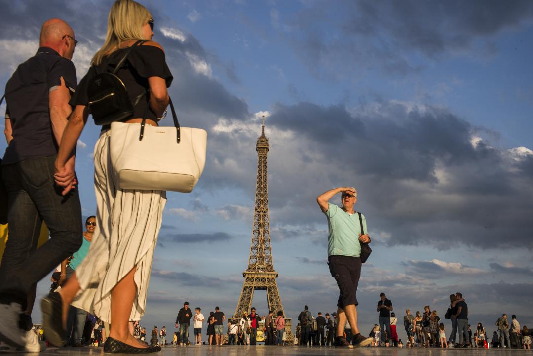 People walk around the Eiffel Tower in Paris, with one couple foregrounded